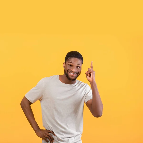 Emozionato ragazzo nero vivendo momento AHA, avendo idea creativa, puntando il dito verso l'alto lo spazio libero su sfondo giallo — Foto Stock