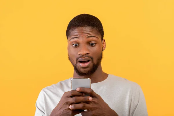 Wow, notizie. Scioccato uomo afro-americano guardando smartphone, leggendo un messaggio sorprendente su sfondo giallo — Foto Stock
