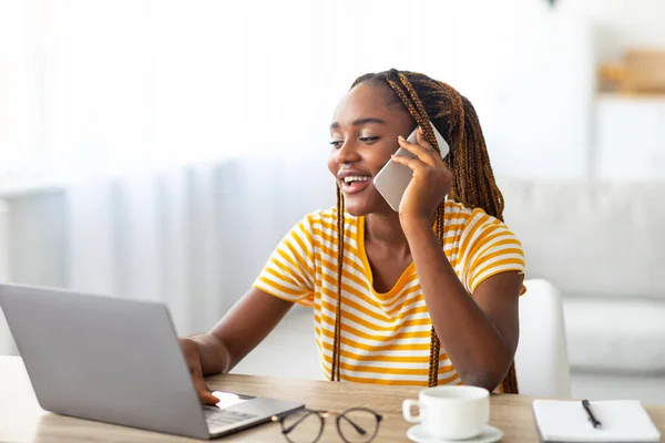 Positieve zwarte vrouw freelancer praten op de telefoon en met behulp van laptop — Stockfoto