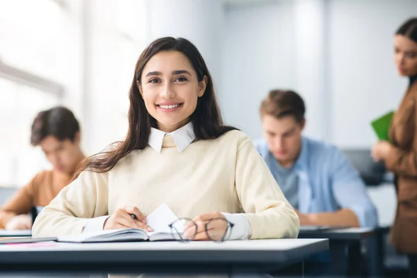 Estudiante sonriente sentado en el escritorio en el aula posando ante la cámara — Foto de Stock