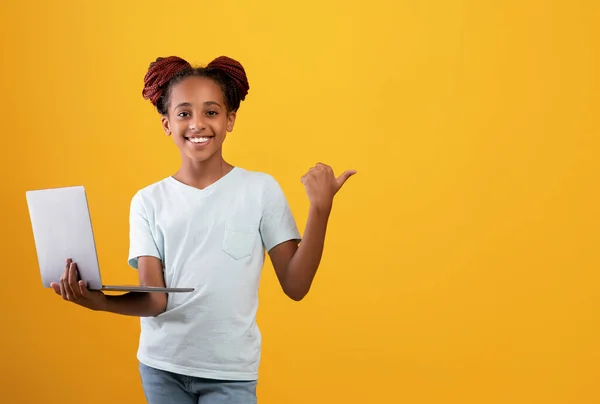 Allegra ragazza adolescente nera con computer portatile che indica lo spazio di copia — Foto Stock