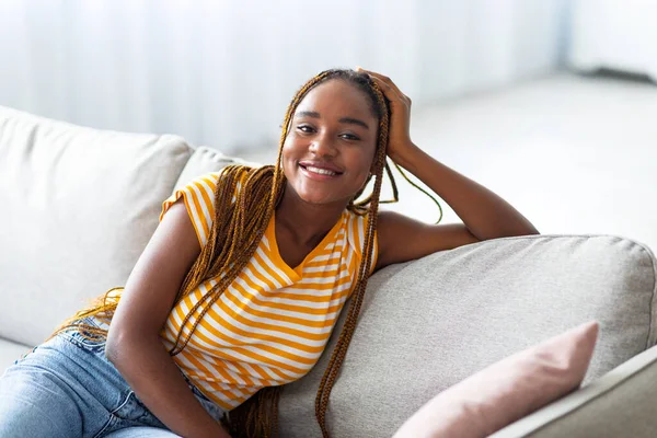 Primer plano de la alegre mujer negra posando en el sofá en casa —  Fotos de Stock