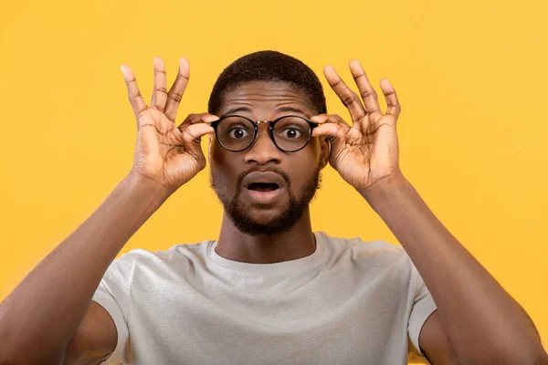 Emocional cara preto tocando seus óculos, gritando WOW no fundo do estúdio amarelo, homem sobrecarregado com grande venda — Fotografia de Stock