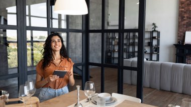 Genç kadın dijital tablet, web veya sosyal medya kullanıyor, çevrimiçi çalışıyor, serbest çalışıyor, evde yeni uygulamaları kontrol ediyor