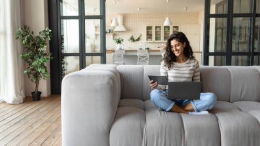 Laptop ve tablet kullanan mutlu beyaz kadın evde online konferans yapıyor, interneti kopyalıyor.