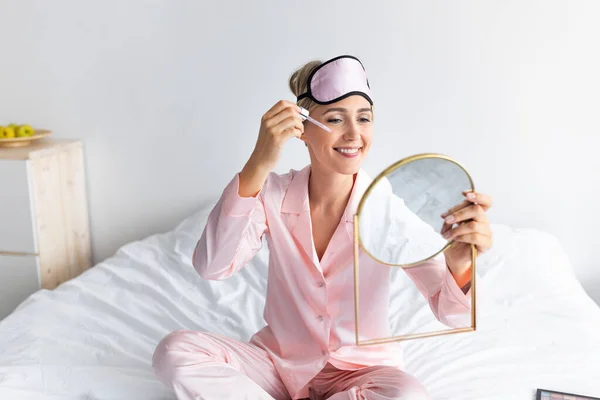 Retrato de mujer sonriente sosteniendo espejo aplicando suero —  Fotos de Stock