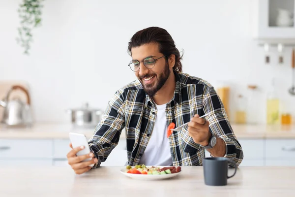 Snygg arabisk man som använder mobiltelefon när han äter frukost — Stockfoto