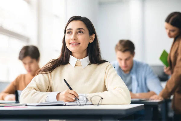 Χαμογελαστή μαθήτρια που κάθεται στο γραφείο στην τάξη και σκέφτεται — Φωτογραφία Αρχείου