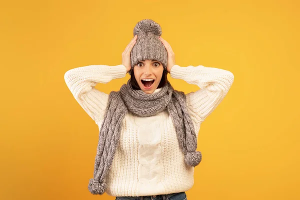 Wow, wat een mooie deal. Vrolijke dame met gebreide muts en sjaal kijkend naar de camera met open mond, gele achtergrond — Stockfoto