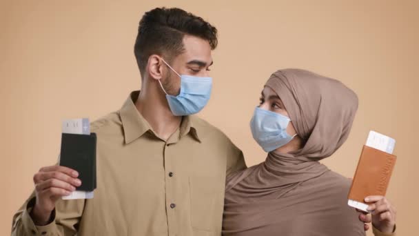 Исламская пара в масках, держащая билеты на самолет на бежевом фоне — стоковое видео
