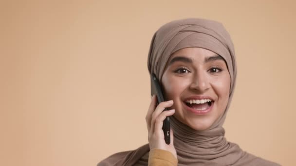 Hembra musulmana feliz hablando por teléfono en un fondo beige — Vídeo de stock