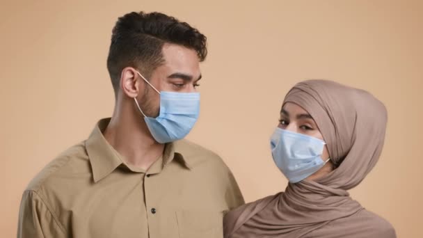 Muslimske par med beskyttende ansiktsmasker med Beige-bakgrunn – stockvideo