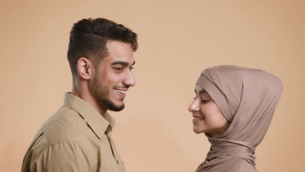 Pareja musulmana girando cabezas y sonriendo de pie sobre fondo beige — Vídeo de stock
