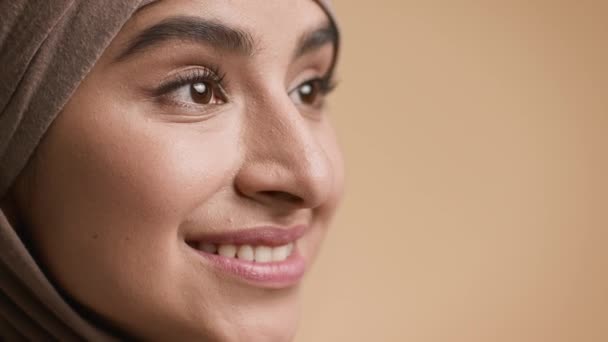 Mujer musulmana en el hiyab sonriendo mirando hacia un lado, fondo beige, primer plano — Vídeo de stock