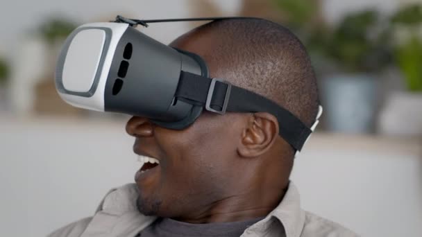 Homem negro excitado vestindo óculos VR experimentando a realidade virtual dentro de casa — Vídeo de Stock