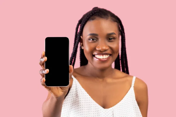 Веселая черная леди показывает мобильный телефон с макетом для дизайна на фоне розовой студии — стоковое фото