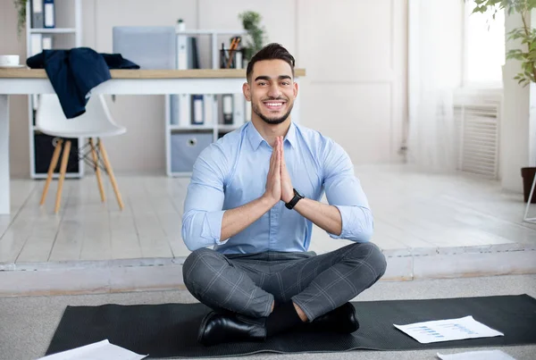 Gestão do stress no local de trabalho. Servidor árabe pacífica meditando, fazendo gesto namaste no tapete de ioga no escritório — Fotografia de Stock