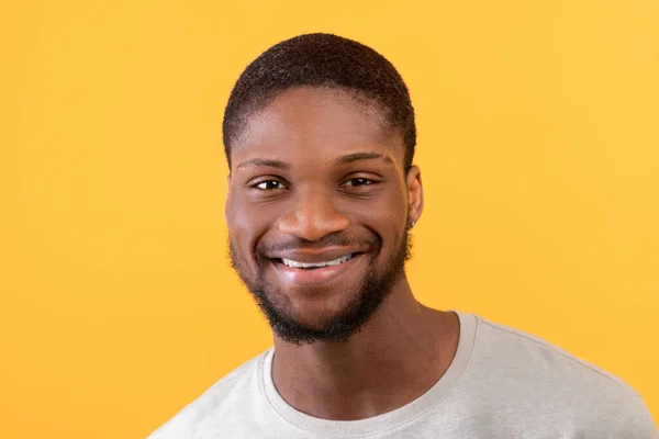 Detailní portrét mladého afrického Američana usmívajícího se do kamery, stojící izolovaně nad žlutým pozadím, volný prostor — Stock fotografie