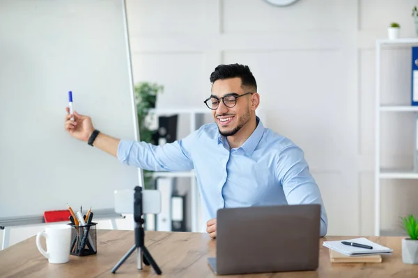 Arabischer männlicher Nachhilfelehrer, der in der Nähe einer leeren Tafel Fernunterricht gibt, mit Geräten für den Fernunterricht zu Hause, Attrappe — Stockfoto