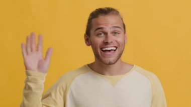Hoş geldiniz. Dost canlısı genç adam el sallıyor ve sarı arka planda duruyor.