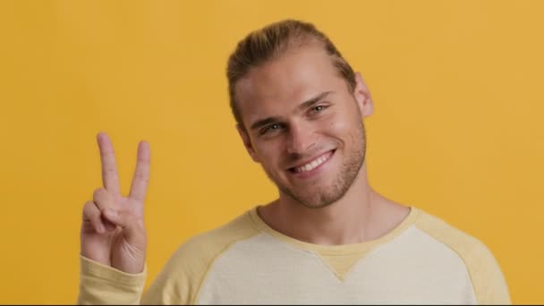 Χαρούμενος νεαρός που δείχνει την ειρηνοληψία ενώ ποζάρει πάνω από το κίτρινο φόντο του στούντιο — Αρχείο Βίντεο