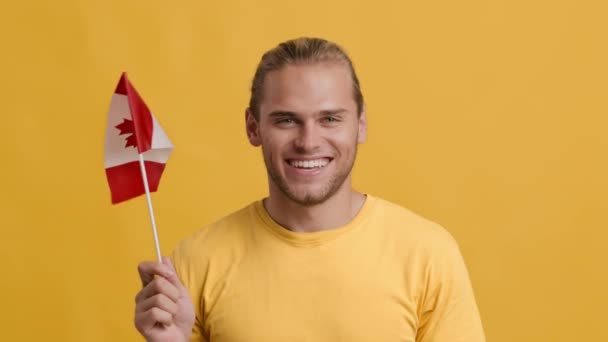 Ung patriotisk man viftar med flagga Kanada och ler mot kameran — Stockvideo