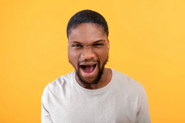 Furia. Arrabbiato ragazzo nero gridando emotivamente alla fotocamera, esprimendo rabbia e aggressività su sfondo giallo — Foto Stock