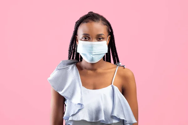 Protecção contra o coronavírus. Jovem mulher negra em máscara protetora médica olhando para a câmera no fundo rosa — Fotografia de Stock