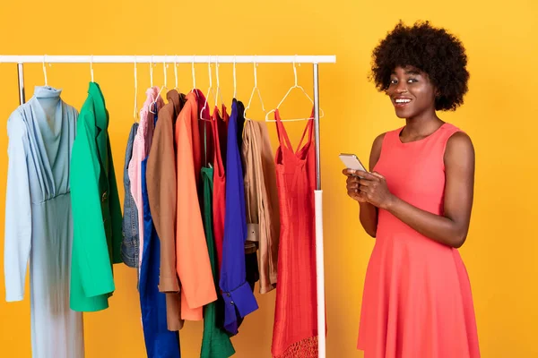 Mulher negra comprando roupas on-line via Smartphone sobre fundo amarelo — Fotografia de Stock