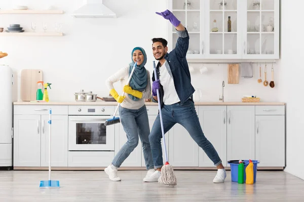 Šťastný muslim pár úklid podlahy a baví v kuchyni — Stock fotografie