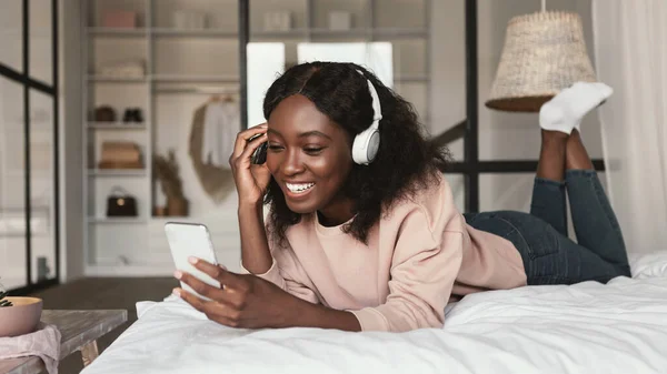 Schwarze Millennial-Frau mit Smartphone trägt Kopfhörer im Schlafzimmer — Stockfoto