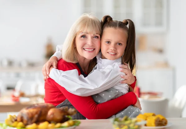 Літня жінка обіймає онуку, готуючи святковий сімейний обід зі смачною індичкою вдома — стокове фото
