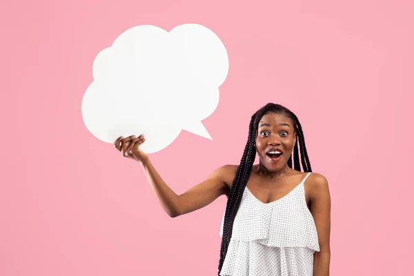 Mujer Afro impactada sosteniendo burbuja de discurso en blanco con maqueta para el diseño de anuncios en fondo de estudio rosa —  Fotos de Stock