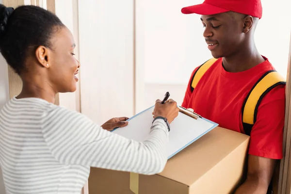 Afrikanerin unterschreibt Zettel, die Paket vom Kurier zu Hause erhält — Stockfoto