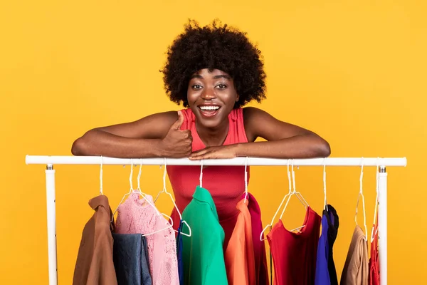 Gelukkig zwart vrouw staande in de buurt van kleding Rail over gele achtergrond — Stockfoto