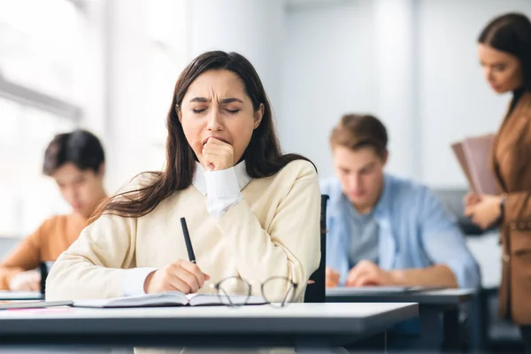 Estudiante bostezando sentada en el escritorio en clase — Foto de Stock