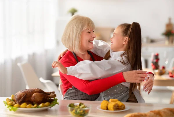 Kochen mit Oma. Entzückendes Mädchen mit Großmutter, die sich umarmt, während sie gemeinsam in der Küche festliches Essen zubereitet — Stockfoto