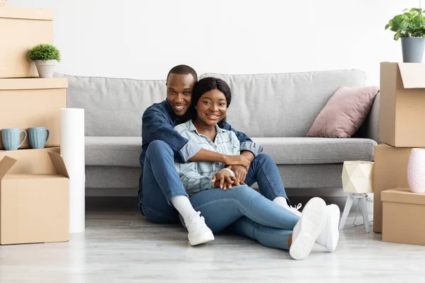 Χαρούμενο αφροαμερικάνικο ζευγάρι που κάθεται στο δωμάτιο με χαρτόκουτα την ημέρα της μετακόμισης — Φωτογραφία Αρχείου