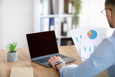 Tanımlanamayan Arap işadamı şirket ofisinde boş ekranla dizüstü bilgisayarda çalışıyor, web sitesi için modelleme yapıyor