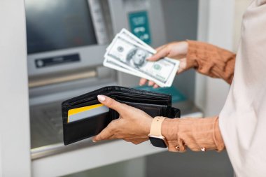 Genç Arap kadın ATM makinesinden dolar almış, dışarıda cüzdanda para katlıyor, kırpılmış.