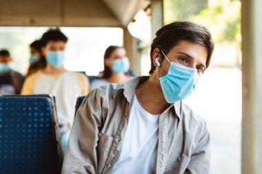 Maskeli genç adam otobusla müzik dinliyor.