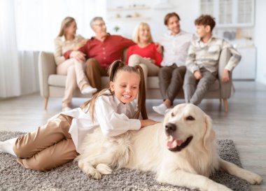 Oturma odasında Golden Retriever köpeğiyle oynayan sevimli bir kız. Akrabaları evdeki kanepede dinleniyor.