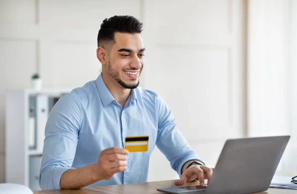 Vrolijke Arabische man met laptop computer en creditcard kopen via internet op kantoor — Stockfoto