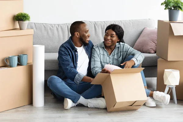 Счастливая чёрная пара переезжает в новую квартиру, распаковывает картонные коробки с принадлежностями — стоковое фото