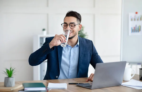 現代のオフィスでラップトップで作業しながらスーツ飲料水でクールなアラブのビジネスマン — ストック写真