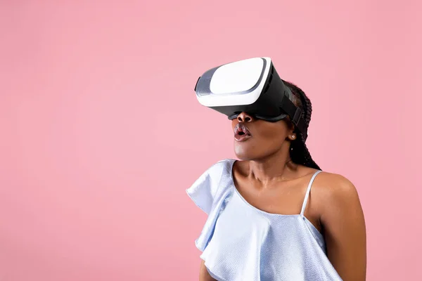 Surprised black lady in VR glasses exploring cyberspace, playing online game in virtual reality on pink background — Stock Photo, Image