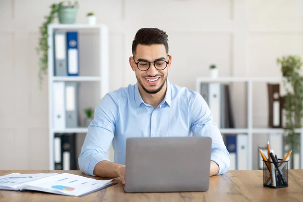Porträt eines selbstbewussten jungen Arabers, der mit Laptop an seinem Tisch sitzt und im Büro auf der Tastatur tippt — Stockfoto