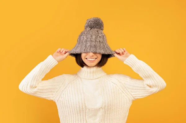 Overblijde dame trekken naar beneden grijze wollen hoed en glimlachen, gek en poseren voor de camera over gele achtergrond — Stockfoto