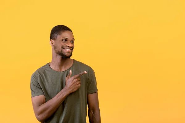 Cara preto positivo sorrindo e apontando para o espaço livre, isolado sobre fundo estúdio amarelo, banner — Fotografia de Stock