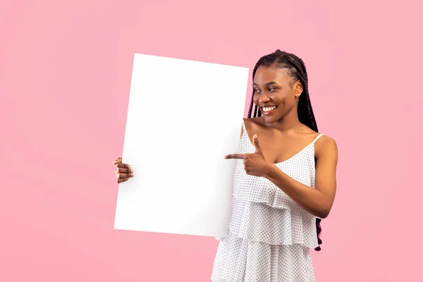 Mulher negra alegre com cachos afro apontando para banner vazio com espaço para design em fundo rosa — Fotografia de Stock